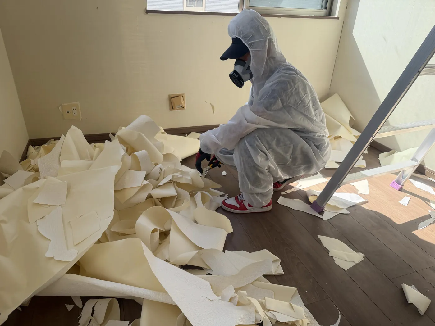 防護服と防毒マスクを着用し、汚れた壁紙(クロス)を剥がす作業